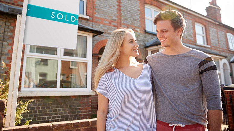 Male and female couple stadning outside their new home with a sold sign